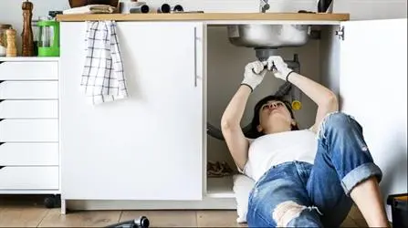 A woman laying under a sink to fix it.