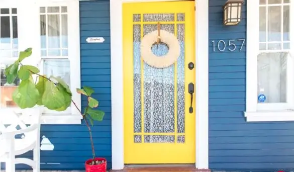 The yellow front door of a blue home with a wreath and windows on both sides.