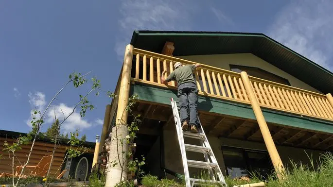 A man on a ladder painting a deck.