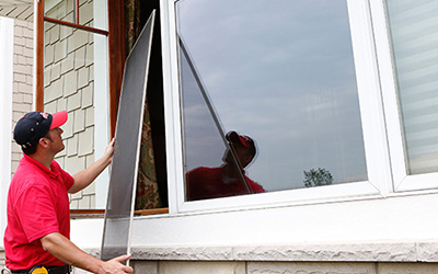 A Mr. Handyman technician installing a screen in a window.