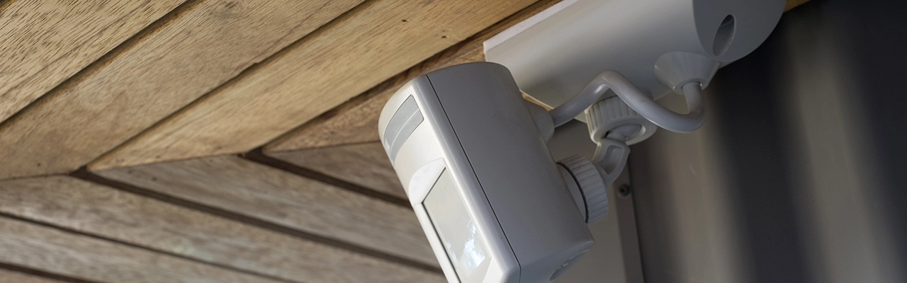 A close-up of a white security camera mounted on a wooden ceiling.