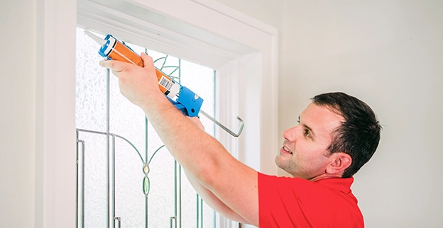 Mr. Handyman technician caulking window.