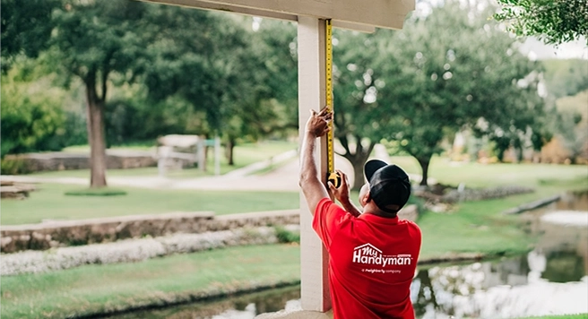 Mr. Handyman technician measuring a porch column with a tape measure.