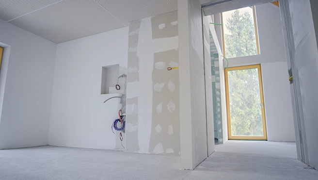 Partially finished room with drywall and construction supplies, featuring large windows and unfinished walls.