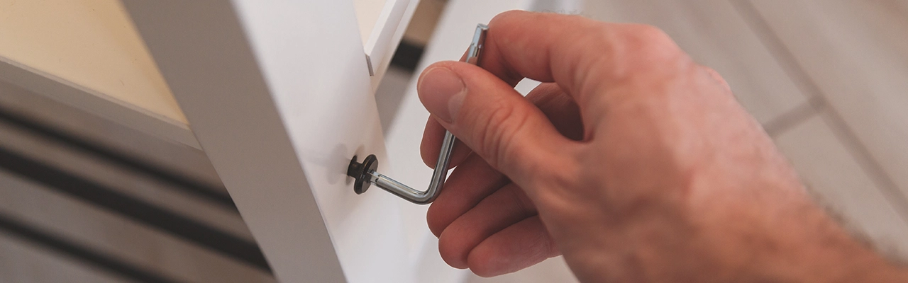 A close-up of a hand using a hex key to fasten a screw on a piece of furniture.
