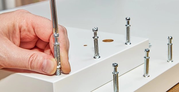 A person tightening a metal screw into a white furniture panel using a screwdriver.