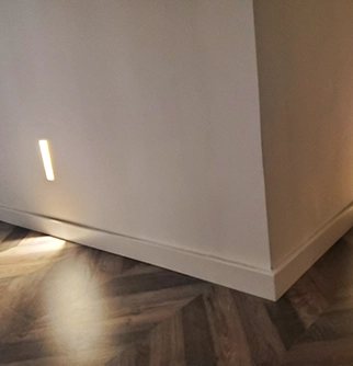 A corner of a room features a sleek white wall with a narrow light strip.