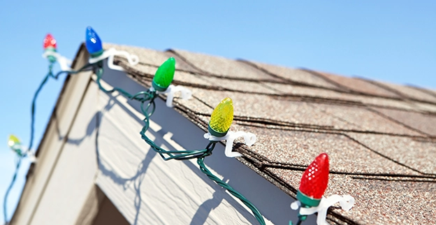 Colorful Christmas lights in blue, green, red, and yellow are strung along a roof's edge.