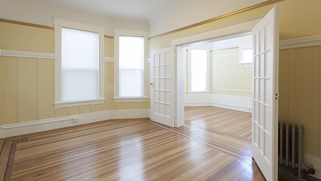 Bright and spacious room with warm wooden floors, textured yellow walls, and large windows.