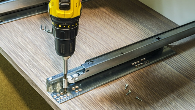 A power drill fastens metal rails to a wooden surface.