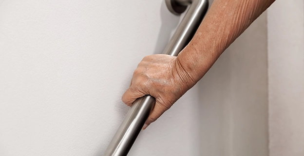 A hand gripping a stainless steel grab bar against a smooth white wall.