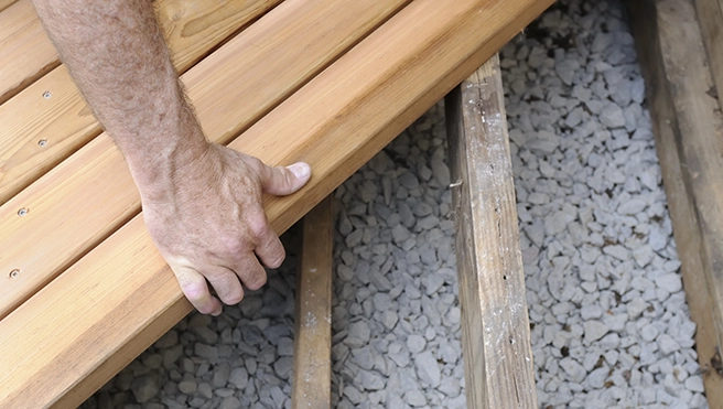 A wooden plank onto a gravel surface, showcasing construction or decking work in progress.