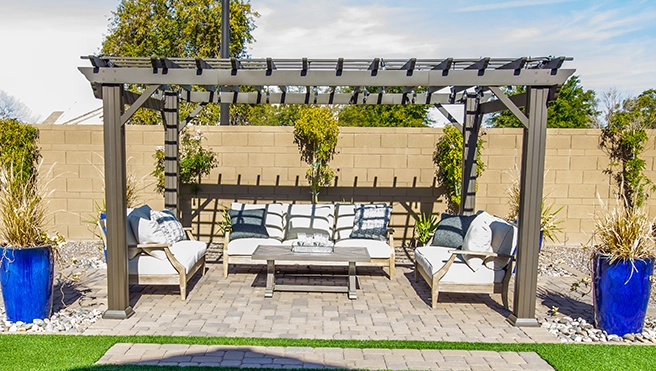 Outdoor patio with a wooden pergola, cozy seating, potted plants, and decorative blue planters against a beige wall.