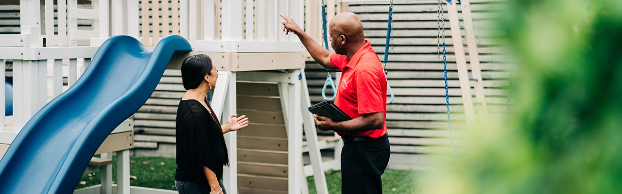 A woman talks with a man in a red shirt near a children's playground.