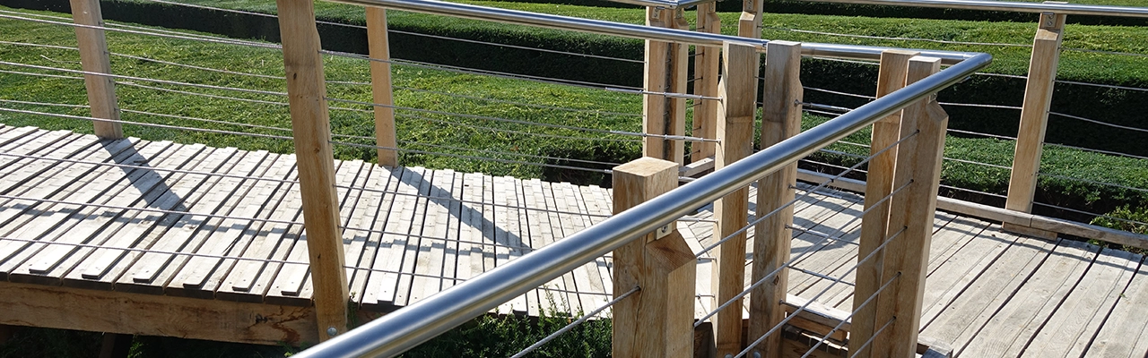 A wooden bridge with metal railings overlooking green hedges.