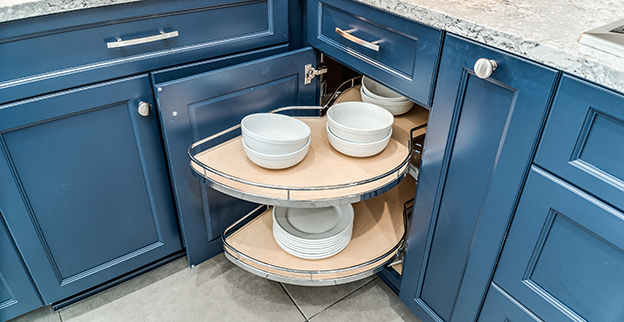 A blue kitchen cabinet with a pull-out, circular shelving unit, displaying stacked white bowls and plates.