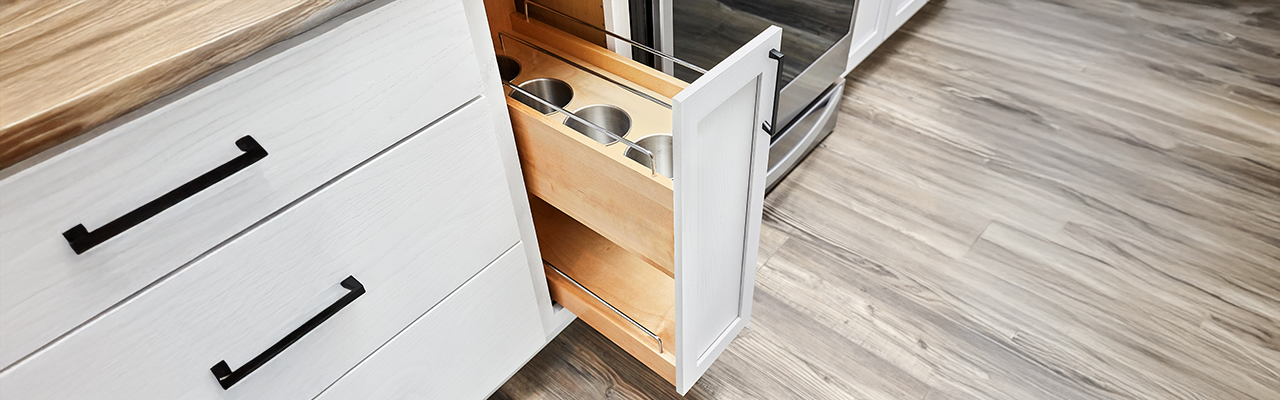 A modern kitchen drawer partially open, revealing wooden shelves with three round metal containers inside.