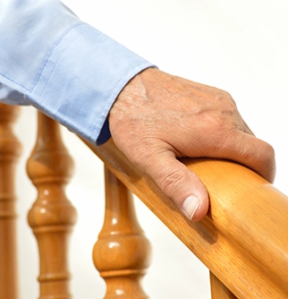 A close-up of a hand resting on a wooden staircase railing.