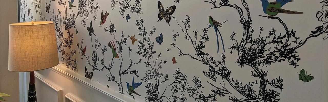 A stylish lamp beside a decorative wallpaper featuring intricate branches, colorful birds, and butterflies.