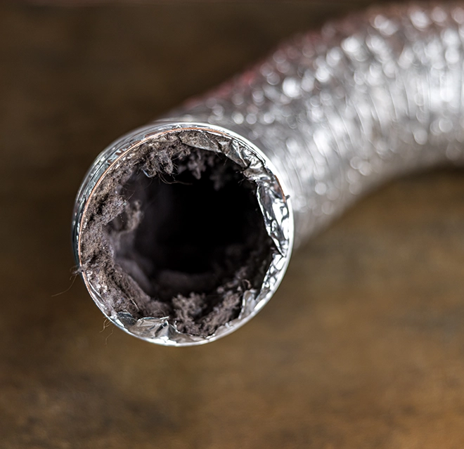 A silver duct with a dark, lint-filled opening, indicating blockage or buildup inside the venting system.