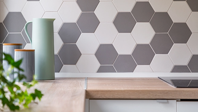 A modern kitchen countertop with a wooden surface featuring green and gray hexagon tiles on the wall, and decorative glass jars.