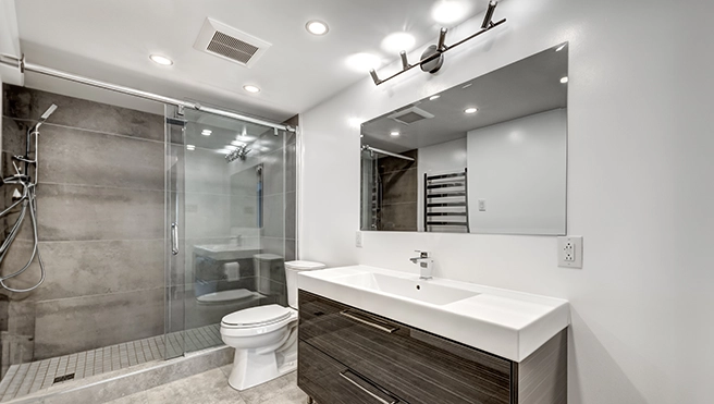 Modern bathroom with a sleek glass shower, dark wood vanity, large mirror, and stylish lighting, featuring neutral-toned tiles.