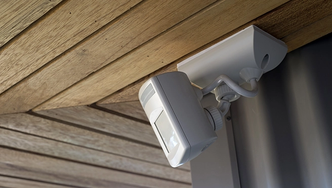 A white surveillance camera mounted on a wooden ceiling.