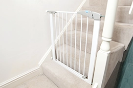 White safety gate installed at the top of a carpeted staircase.