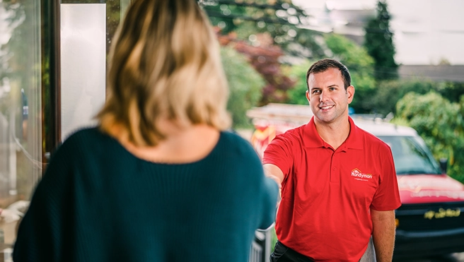 A Mr. Handyman service professional shaking hands with a client on her doorstep.