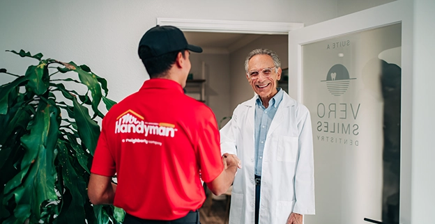 A handyman in a red uniform shakes hands with a doctor.