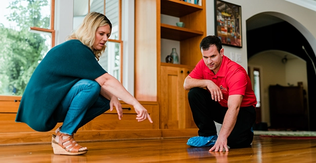 A woman down while discussing something on a wooden floor with a man.