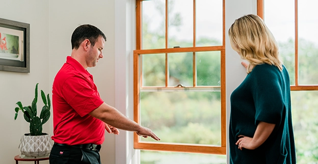 A person towards a window while discussing with a woman, with greenery visible outside.