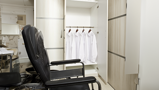 A black chair beside a wardrobe displaying neatly hung white shirts.