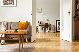 A cozy living room with a beige sofa, orange accent pillow and a wooden coffee table.