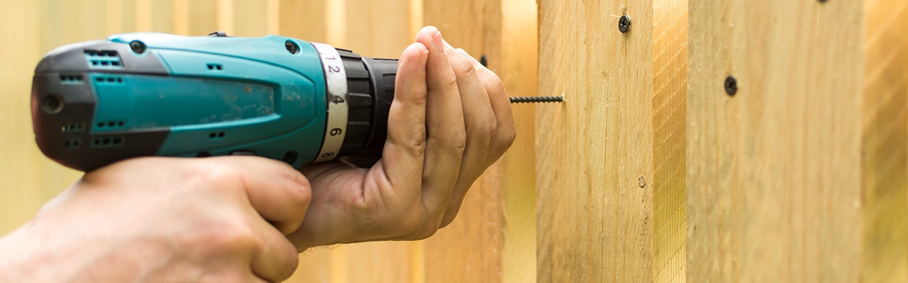 A person uses a power drill to drive a screw into a wooden surface, demonstrating home improvement skills.