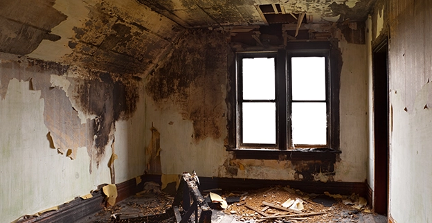 An abandoned room with peeling paint, damaged walls, and a broken chair, illuminated by two dusty windows.