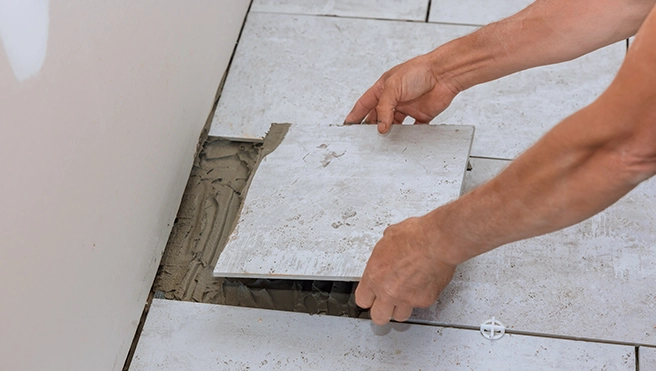 A person places a tile over adhesive on a floor preparing to finish a tiling project.