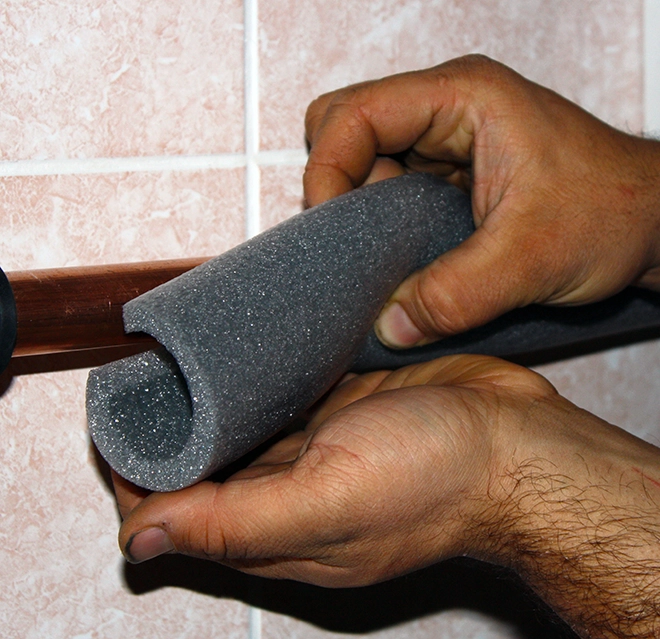 A person insulates a copper pipe with gray foam.