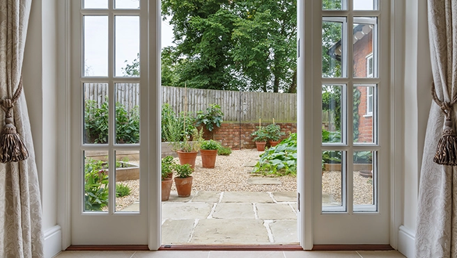 View through French doors into a green garden with potted plants.