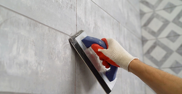 A hand wearing a glove uses a rubber float to apply grout.