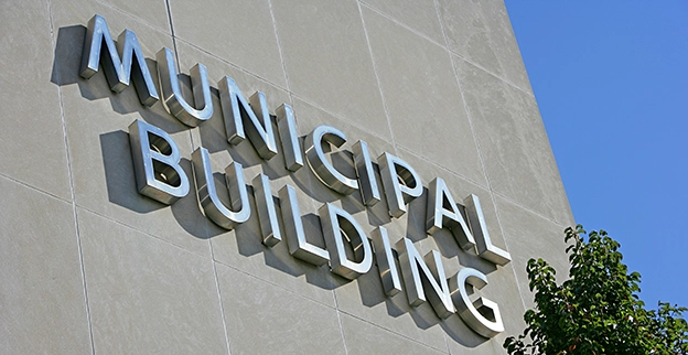 Close-up of the Municipal Building sign mounted on a modern gray wall with greenery partially visible at the bottom right.