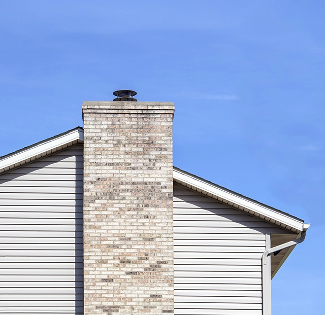 A brick chimney extends from a beige house under a clear blue sky.