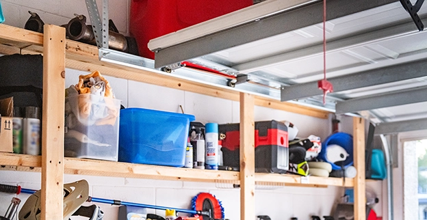 A neatly organized garage shelf filled with various storage bins, tools, and equipment on wooden racks.