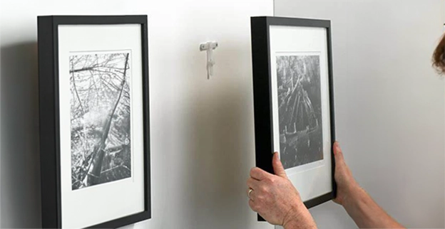 A person hangs two framed black-and-white photographs on a white wall.