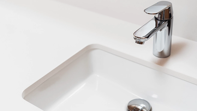 A modern chrome faucet above a clean, white rectangular sink.