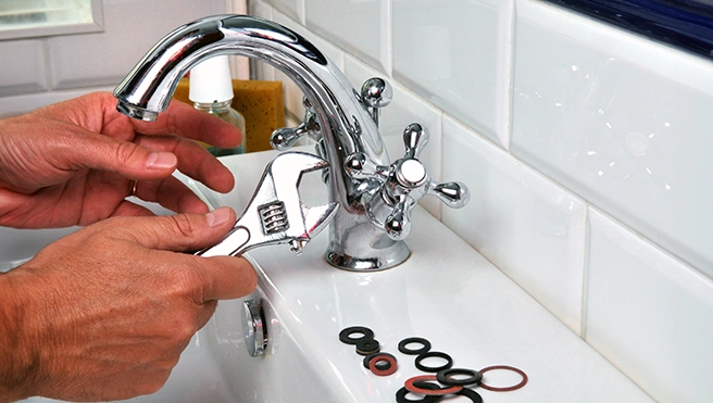 A person uses an adjustable wrench to repair a chrome faucet