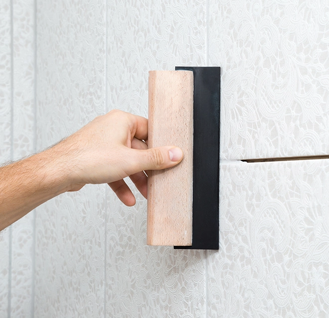 A hand uses a smoothing tool on a textured wall.