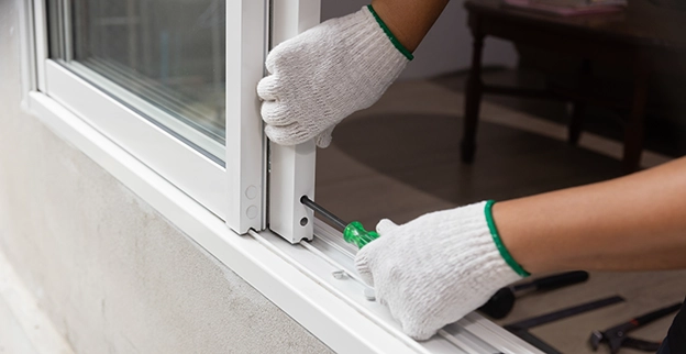 A person wearing gloves is repairing a window using a screwdrive.