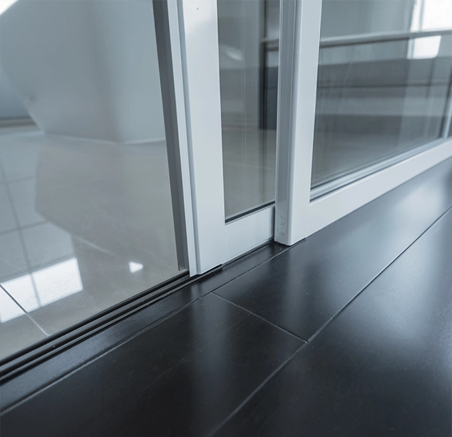 Close-up of a sliding door track, showcasing a sleek transition between dark wooden and light tiled flooring.