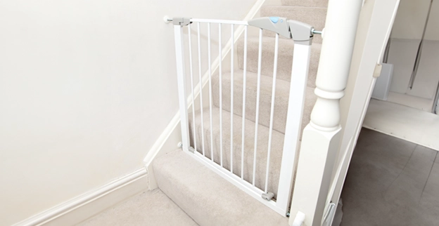A white safety gate installed at the top of a carpeted staircase.